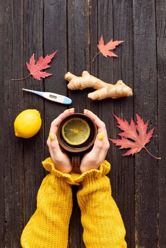 Kubek herbaty w rękach kobiety z cytryną, imbirem i termometrem