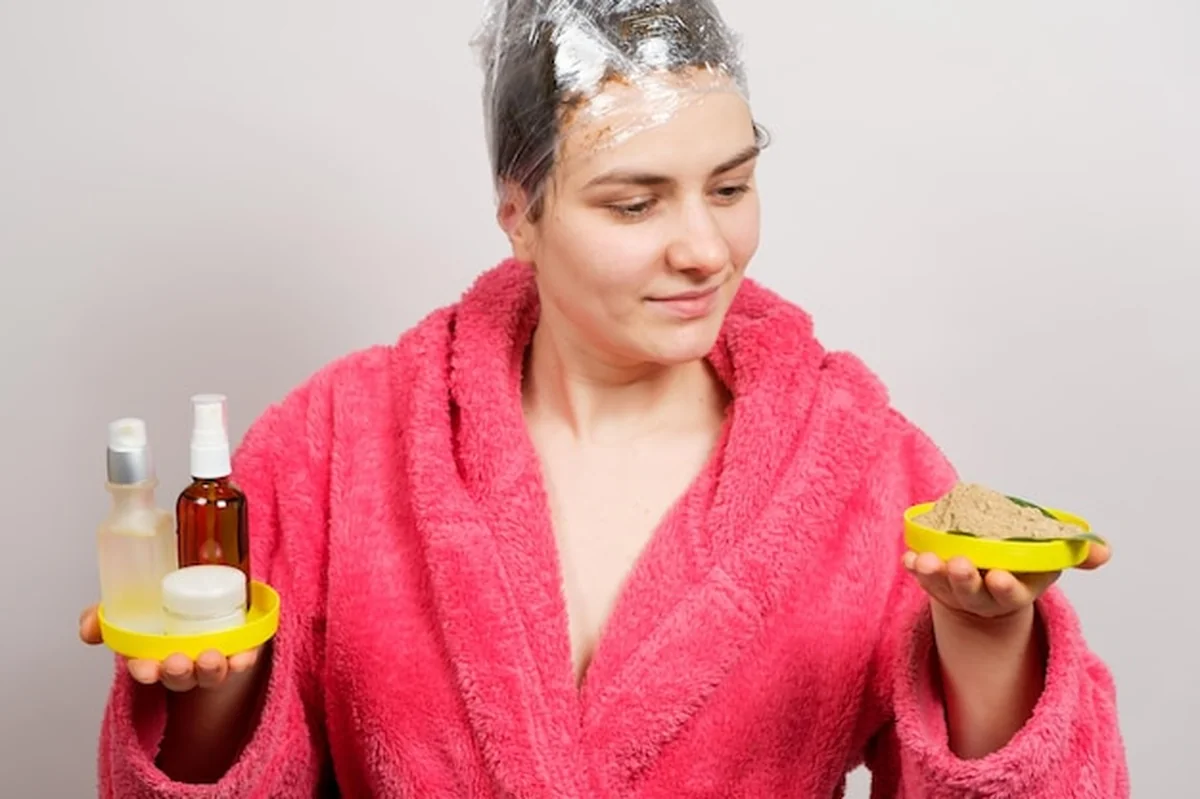 Kobieta z filmem na głowie robi maskę do włosów i trzyma kosmetyki