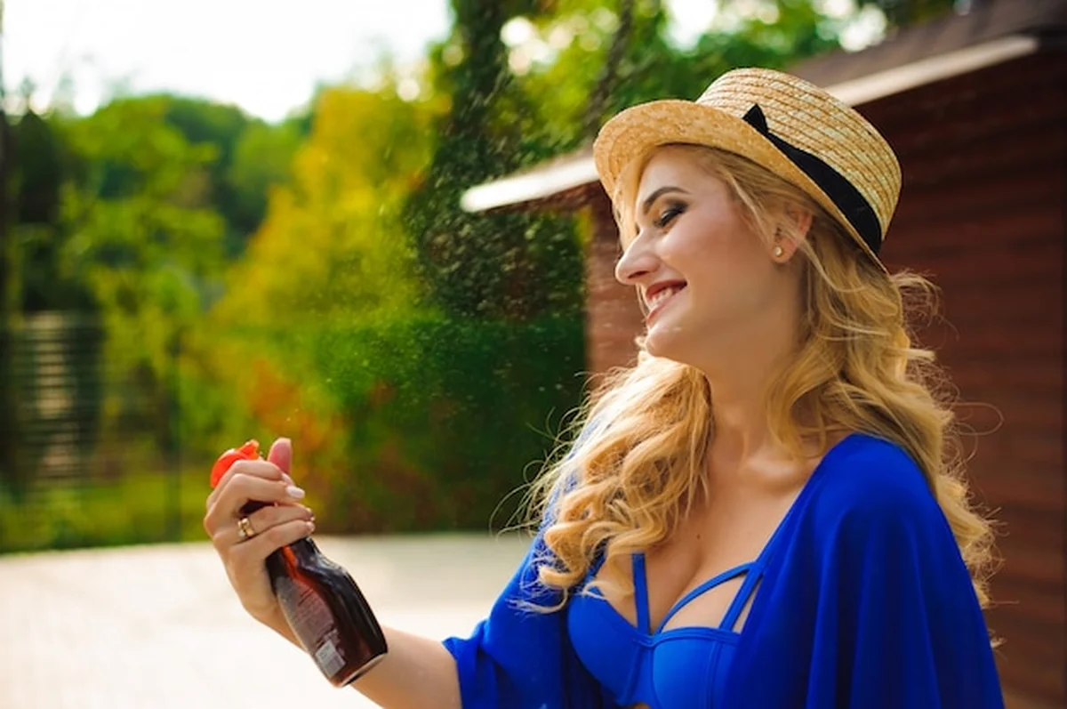 Kobieta w kapeluszu obok basenu z sprayem przeciwsłonecznym