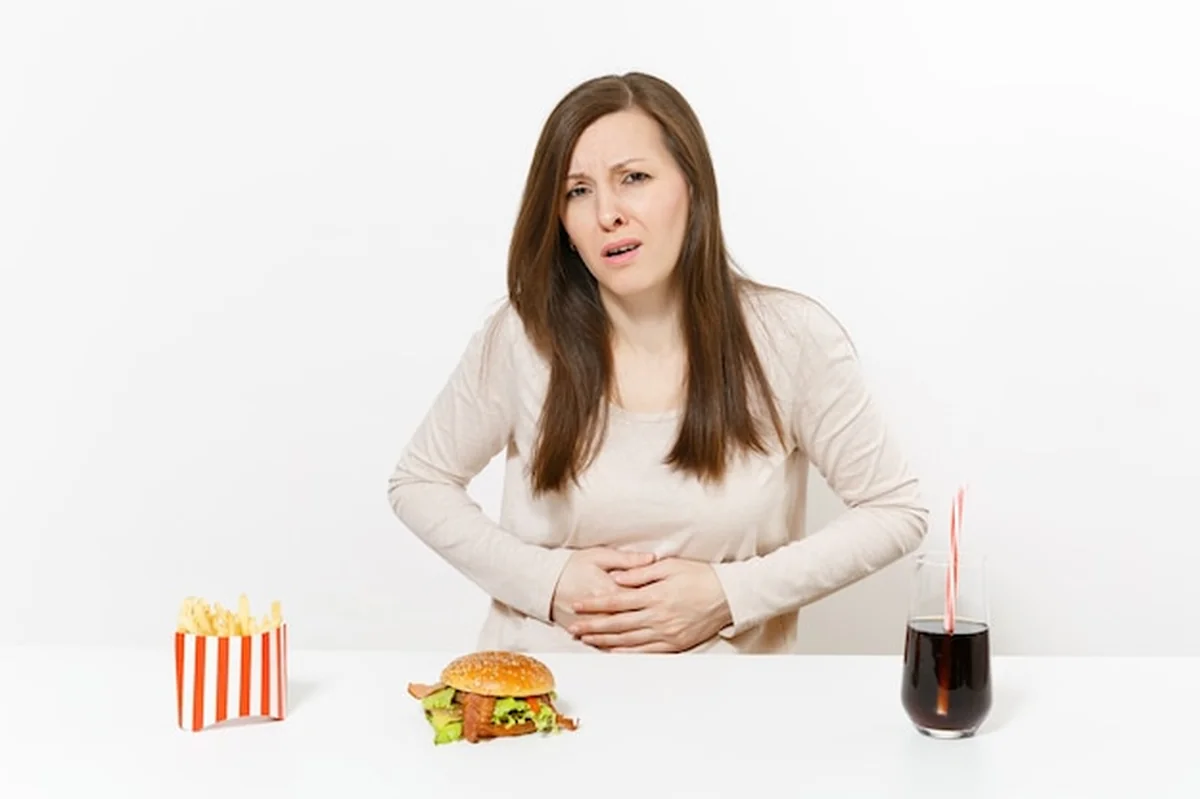 Chora kobieta trzyma brzuch przy stole z fast foodem