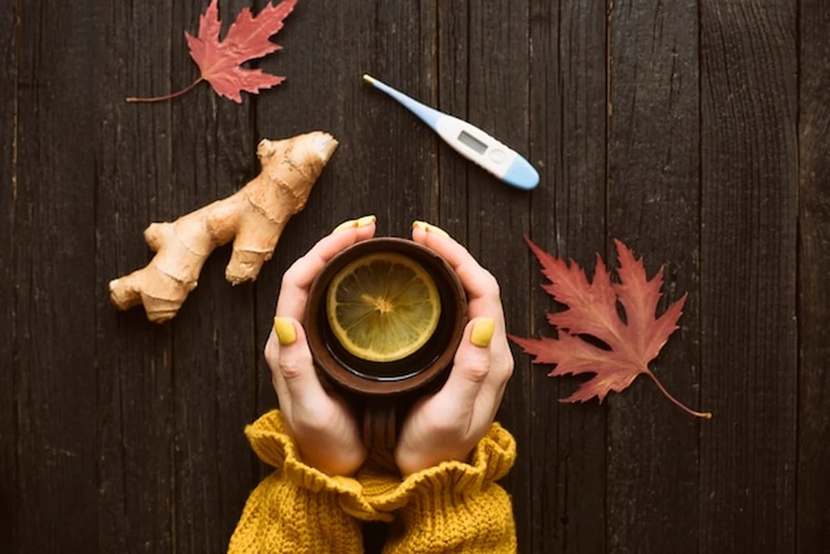 Kubek herbaty w rękach kobiety obok imbiru i termometra