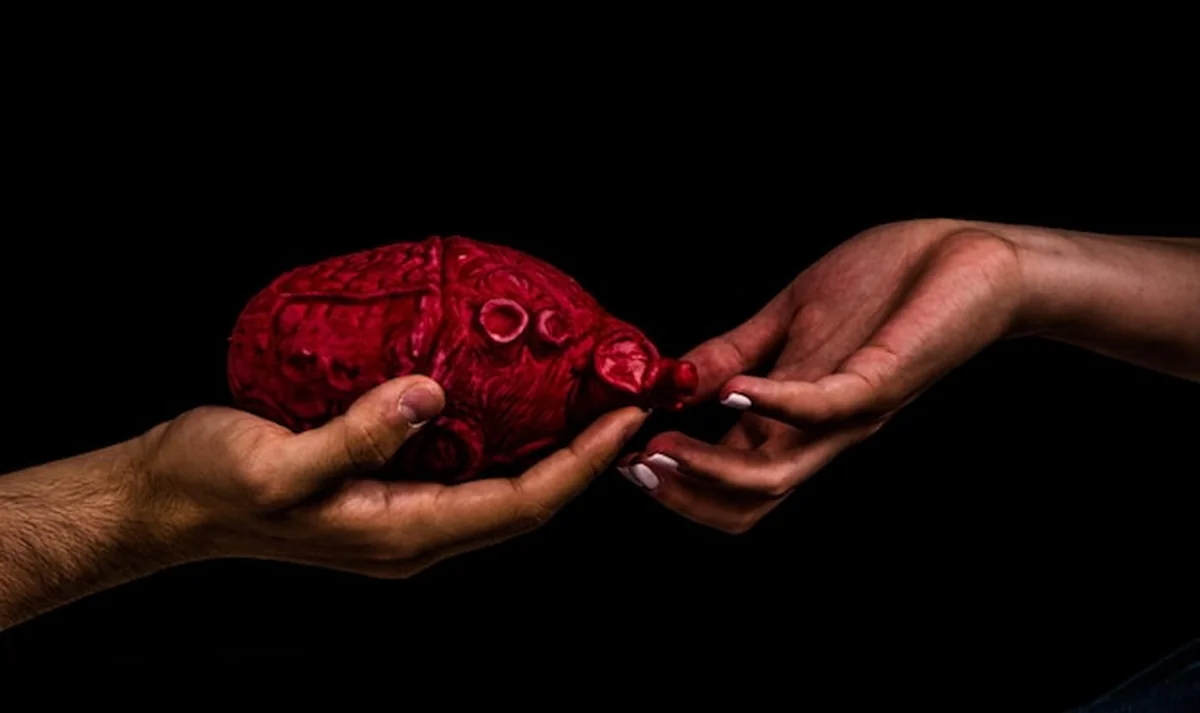 Mężczyzna z odciętą ręką podaje sztuczny mózg kobiecie na czarnym tle