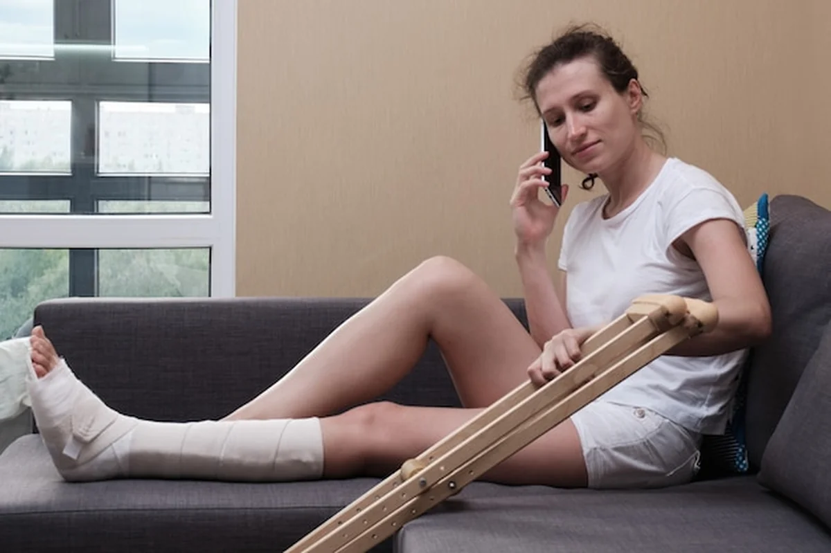 Kobieta w gipsie rozmawia przez telefon na kanapie