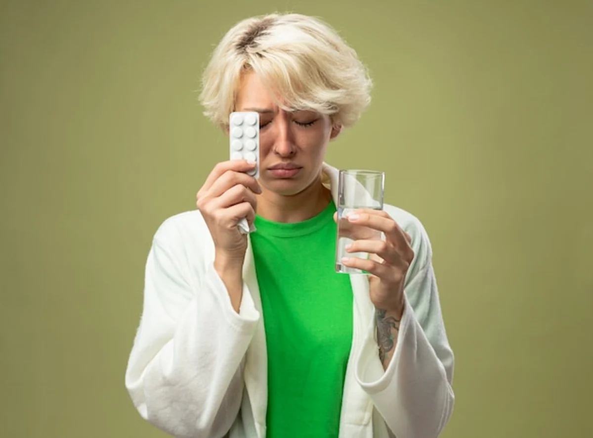 Chora kobieta trzymająca szklankę wody i blister z tabletkami z zamkniętymi oczami