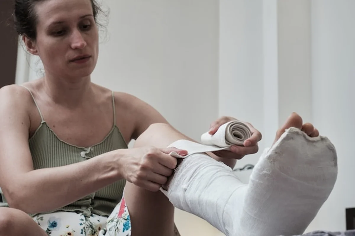 Kobieta siedząca na łóżku zakłada elastyczny bandaż na złamaną nogę
