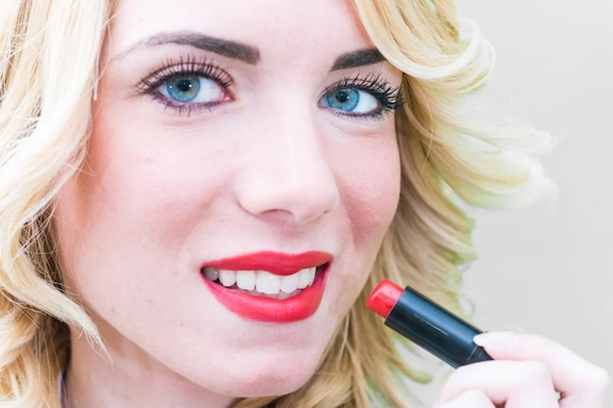 Kobieta nakładająca czerwoną szminkę na szarym tle
