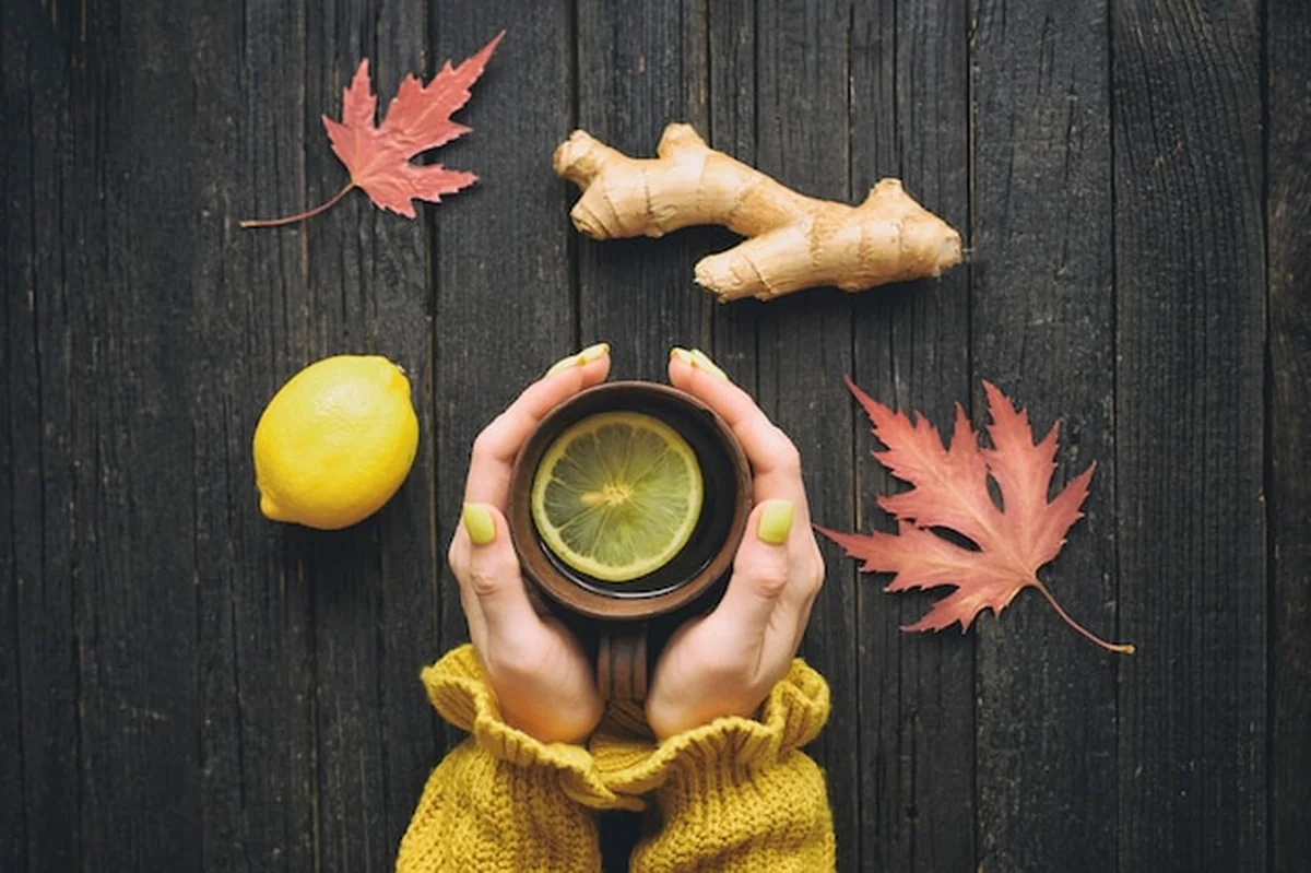 Kubek herbaty w rękach kobiet z imbirem i cytryną, jesienne liście na stole
