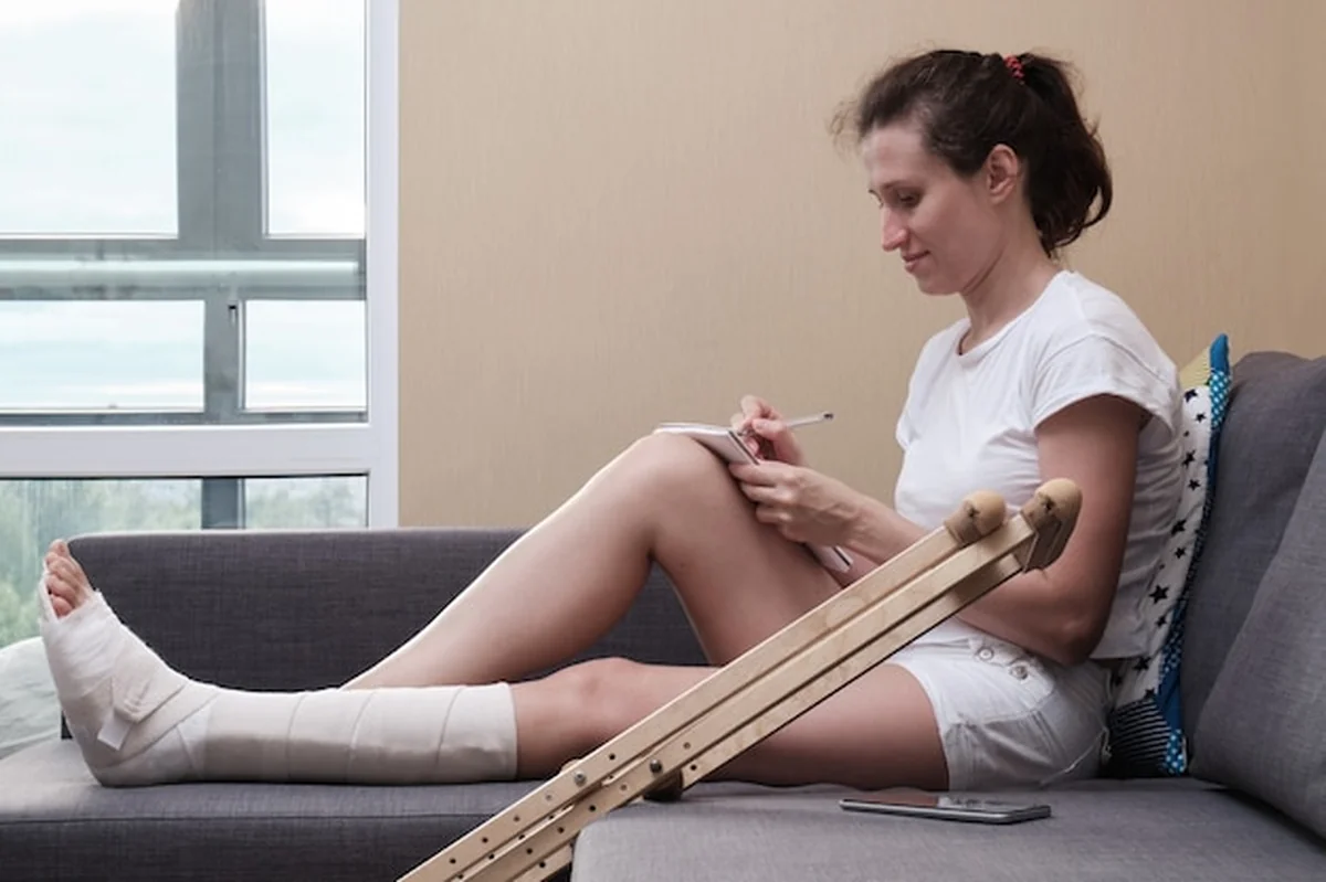 Kobieta w gipsie, pisząca w notesie, siedząca na kanapie w salonie