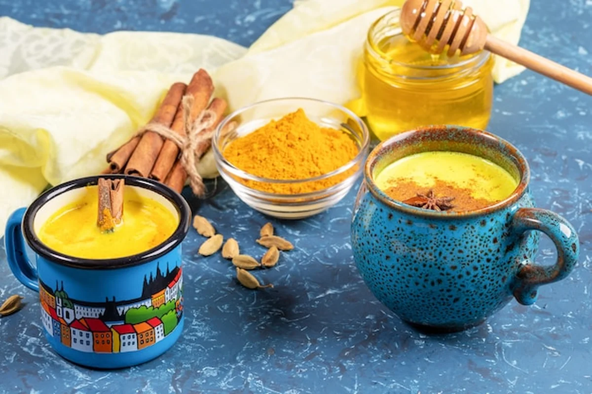 Złote mleko kurkumowe w filiżankach i składniki na serwetce