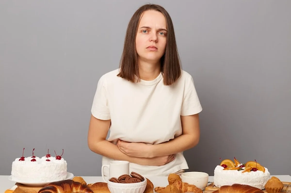 Kobieta z brązowymi włosami jedząca słodką pieczeń, odczuwająca ból brzucha