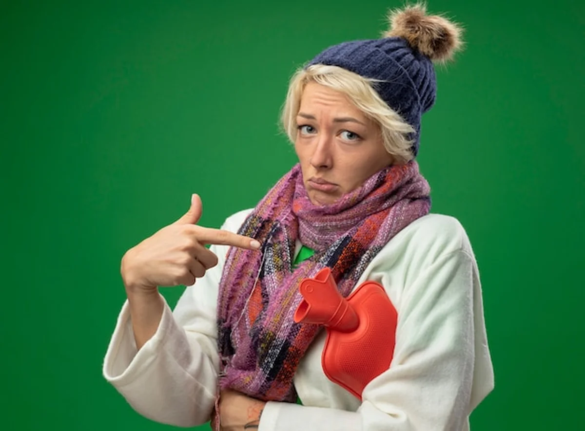 Chora kobieta z termometrem, źle się czująca w ciepłym szaliku i czapce na zielonym tle