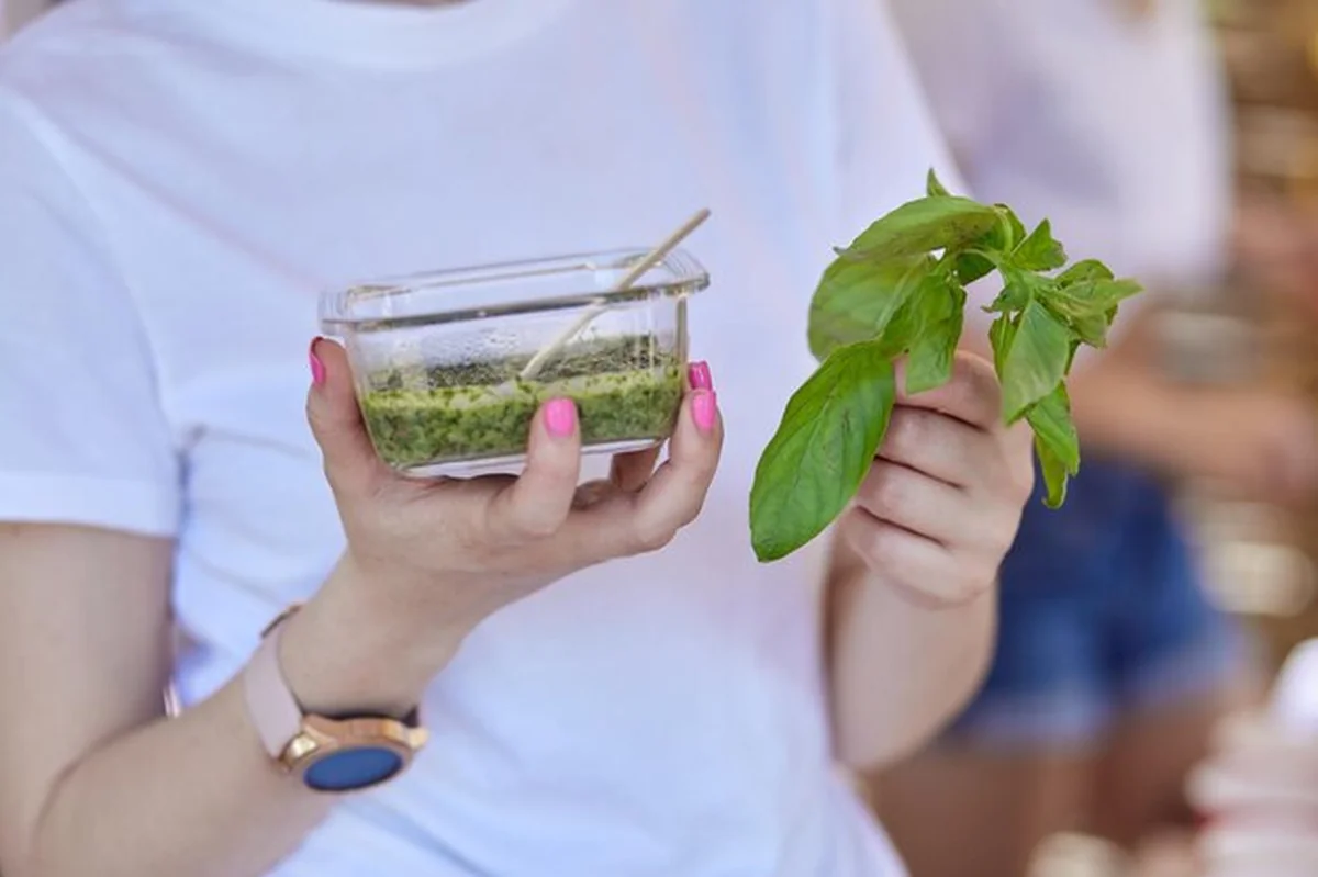 Młoda kobieta trzyma domowy sos pesto i bazylie