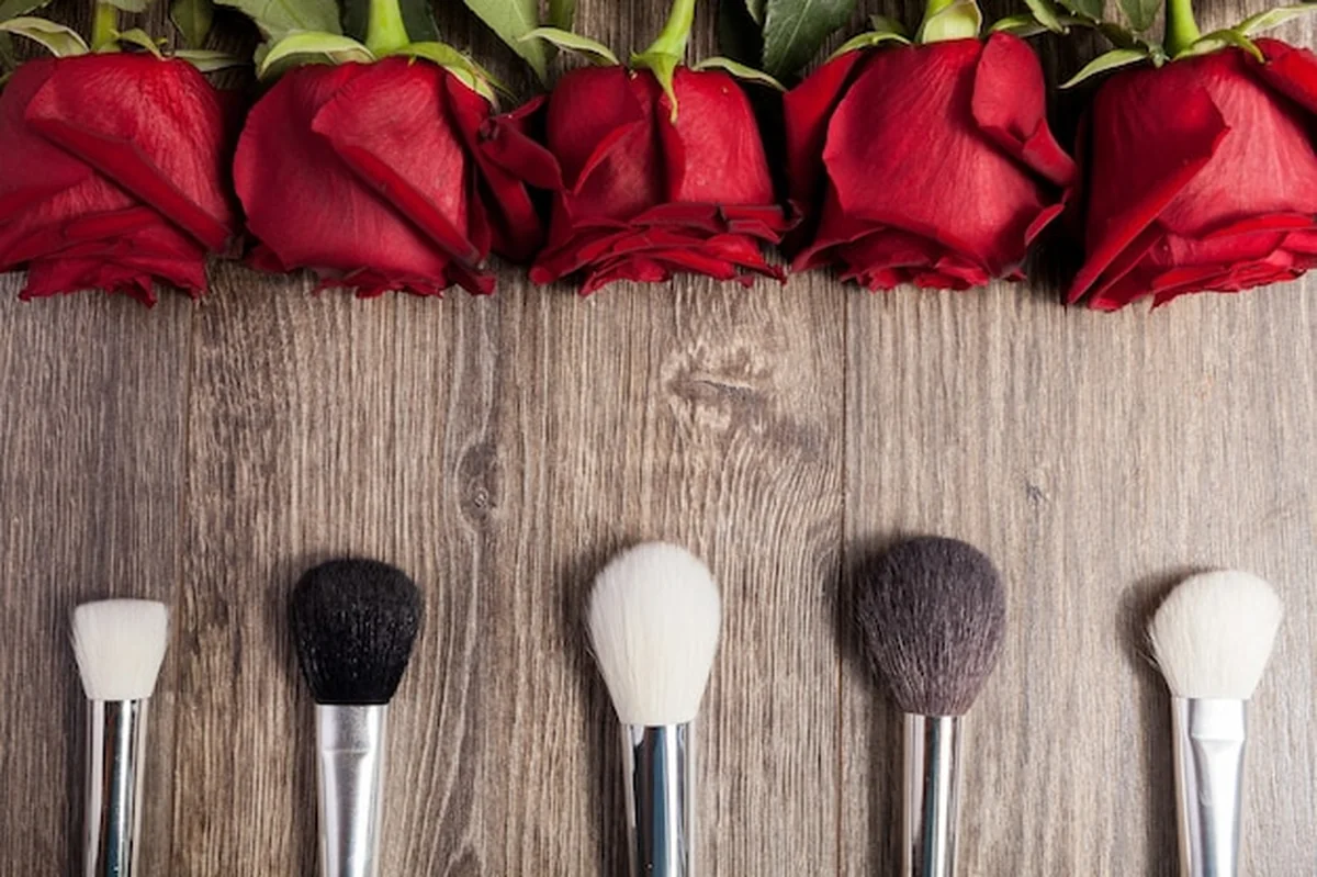 Pędzle do makijażu obok róż na drewnianym tle